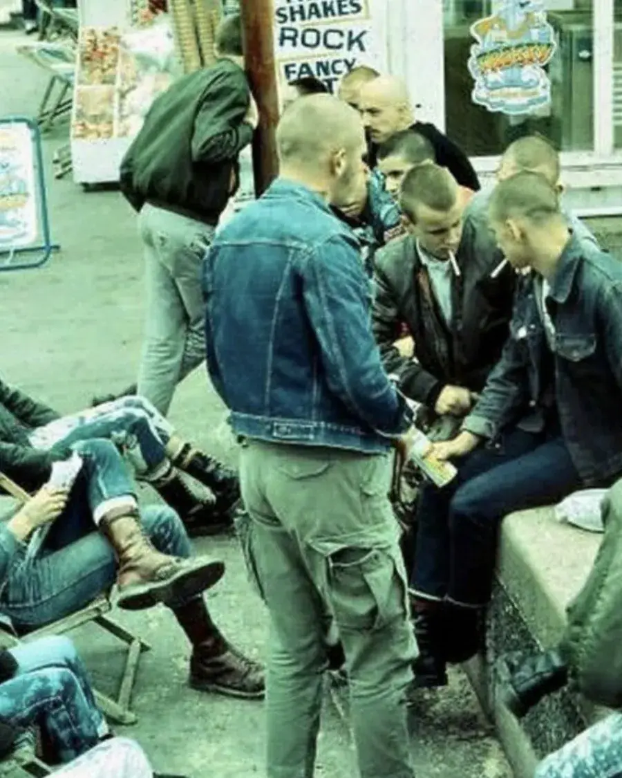 Gruppo di giovani skinhead in giacche di jeans, seduti e in piedi davanti a un chiosco sul lungomare. Foto d'archivio.